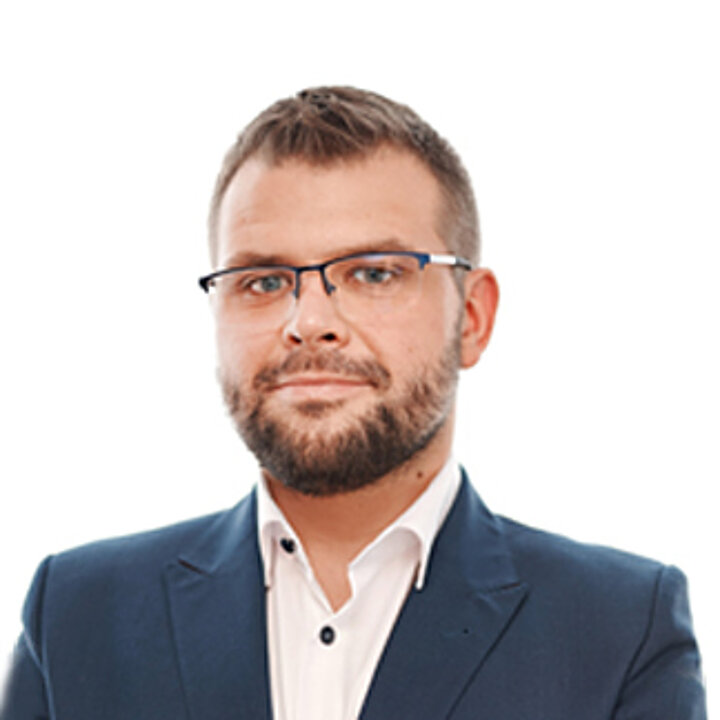 A middle-aged man with a beard and glasses. He wears a navy blue jacket