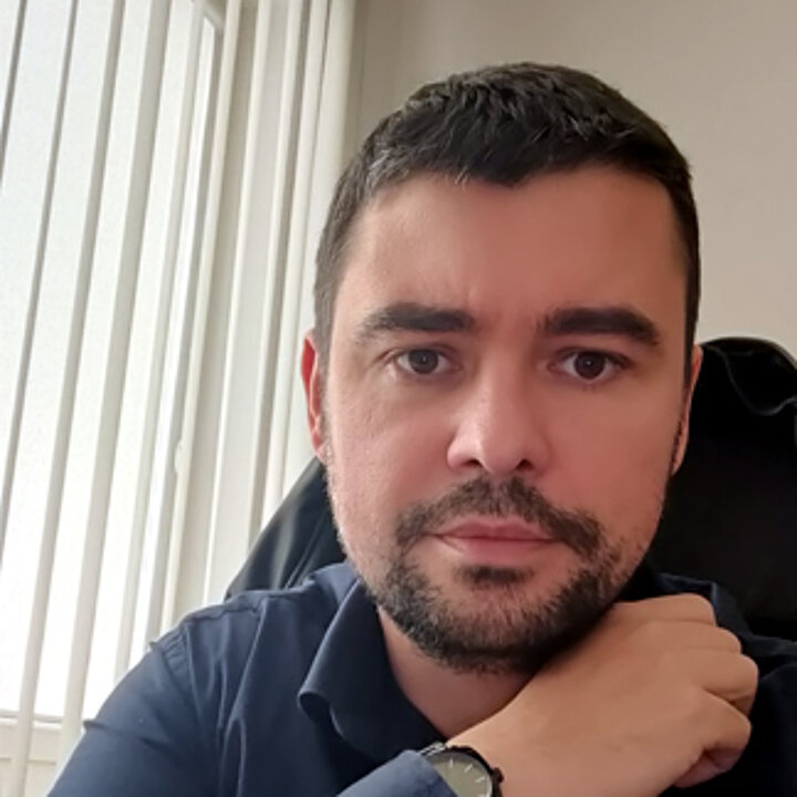 A middle-aged man with a dark beard. He wears a navy blue shirt