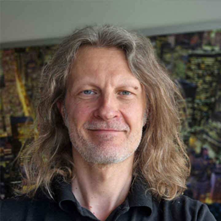 Smiling man with long, slightly graying hair. He wears a black shirt